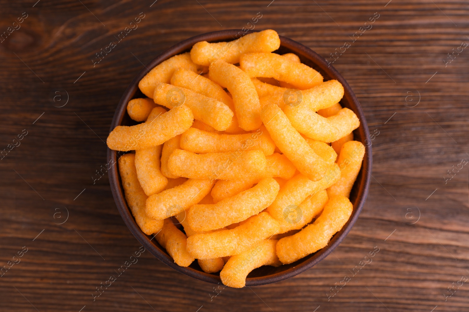 Photo of Bowl with crunchy cheesy corn snack on wooden table, top view