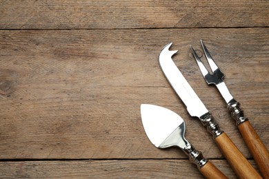 Cheese knives and fork on wooden table, flat lay. Space for text