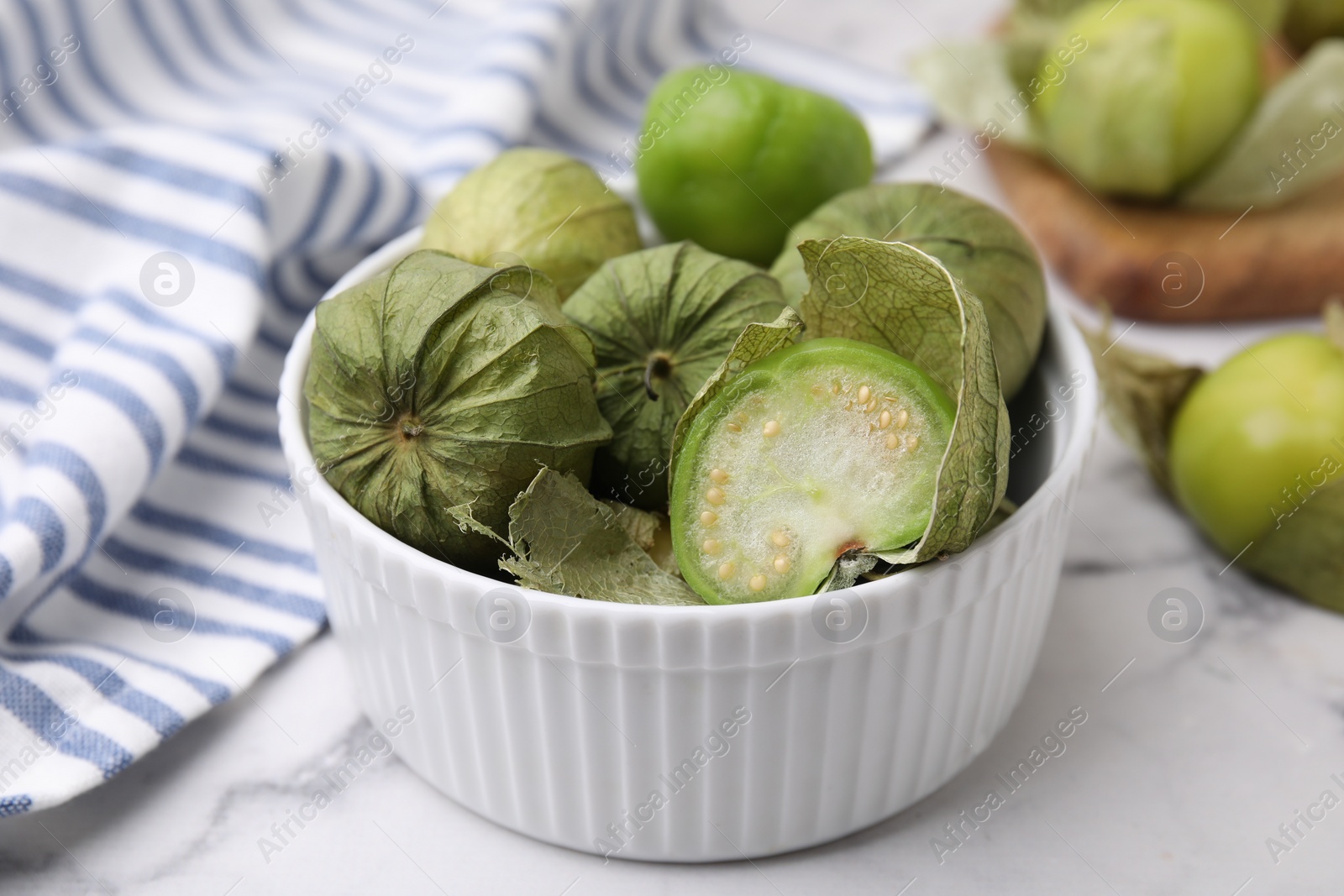 Photo of Fresh green tomatillos with husk in bowl on light marble table, closeup