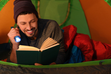 Photo of Man with flashlight reading book in tent