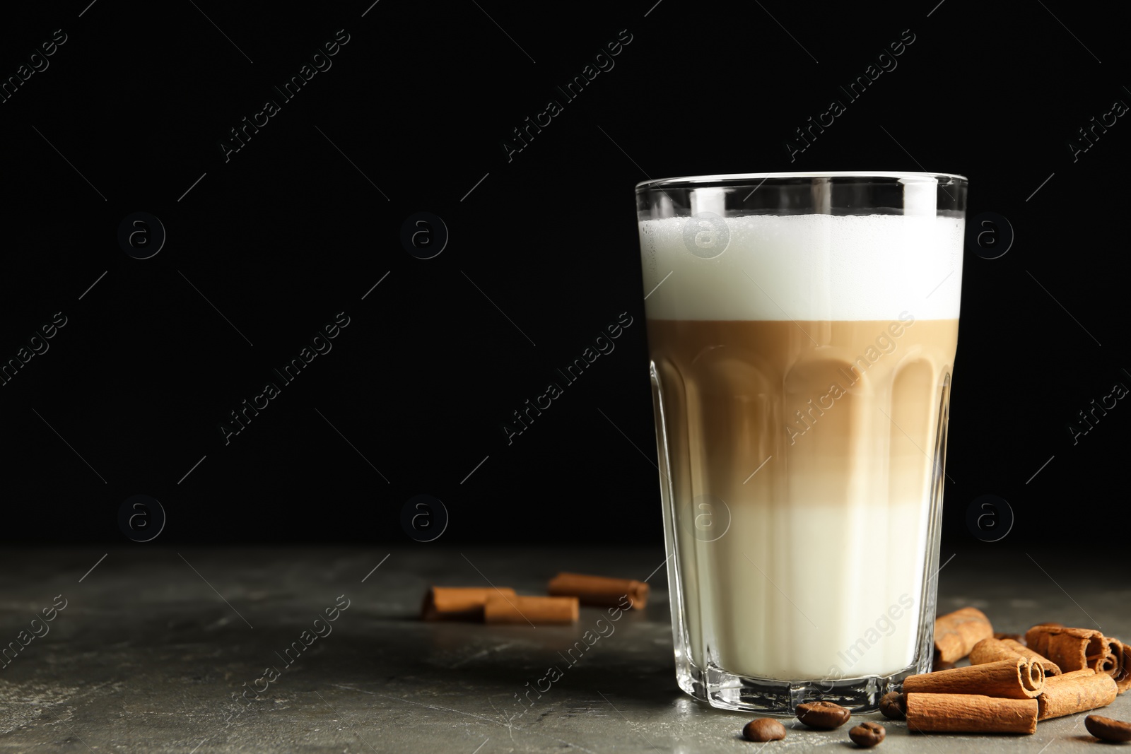 Photo of Delicious latte macchiato and cinnamon on grey table against black background, space for text