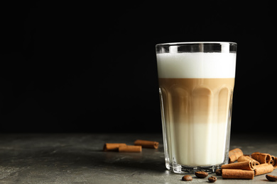 Photo of Delicious latte macchiato and cinnamon on grey table against black background, space for text