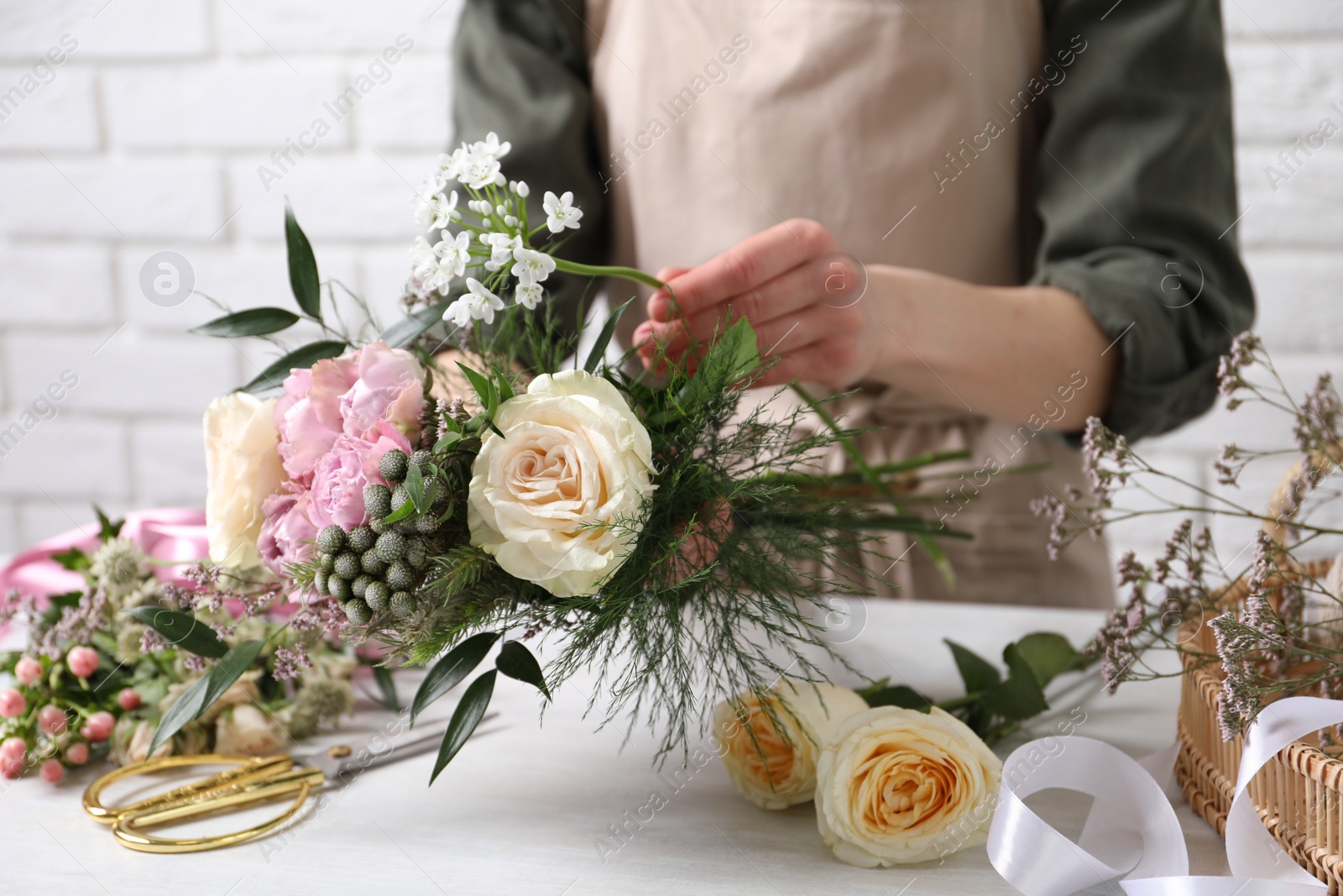Photo of Florist making beautiful bouquet at white table, closeup