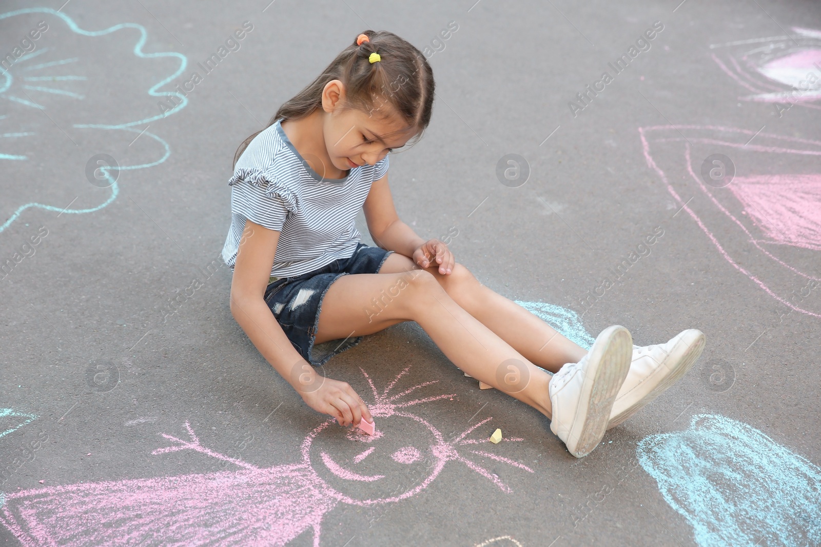 Photo of Little child drawing with colorful chalk on asphalt