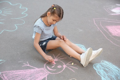 Little child drawing with colorful chalk on asphalt