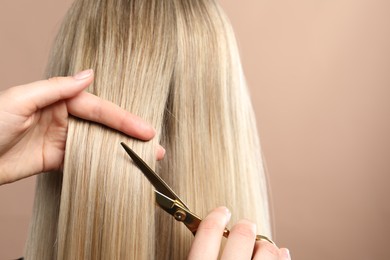 Photo of Hairdresser cutting client's hair with scissors on beige background, closeup. Space for text