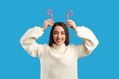 Photo of Young woman in beige sweater holding candy canes on blue background. Celebrating Christmas