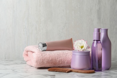 Different hair products, towel and comb on white marble table. Space for text
