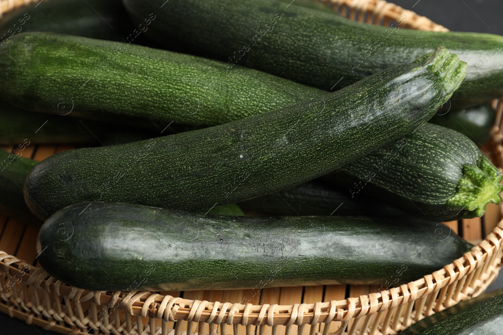 Photo of Green zucchinis in wicker basket, closeup view