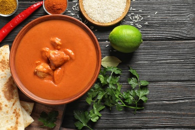 Photo of Delicious butter chicken served on wooden table, top view with space for text. Traditional indian Murgh Makhani