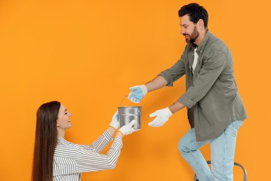 Photo of Woman giving man can of paint near orange wall. Interior design