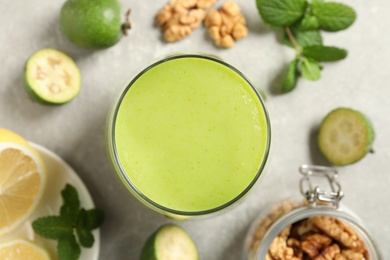 Fresh feijoa smoothie in glass on light grey table, flat lay