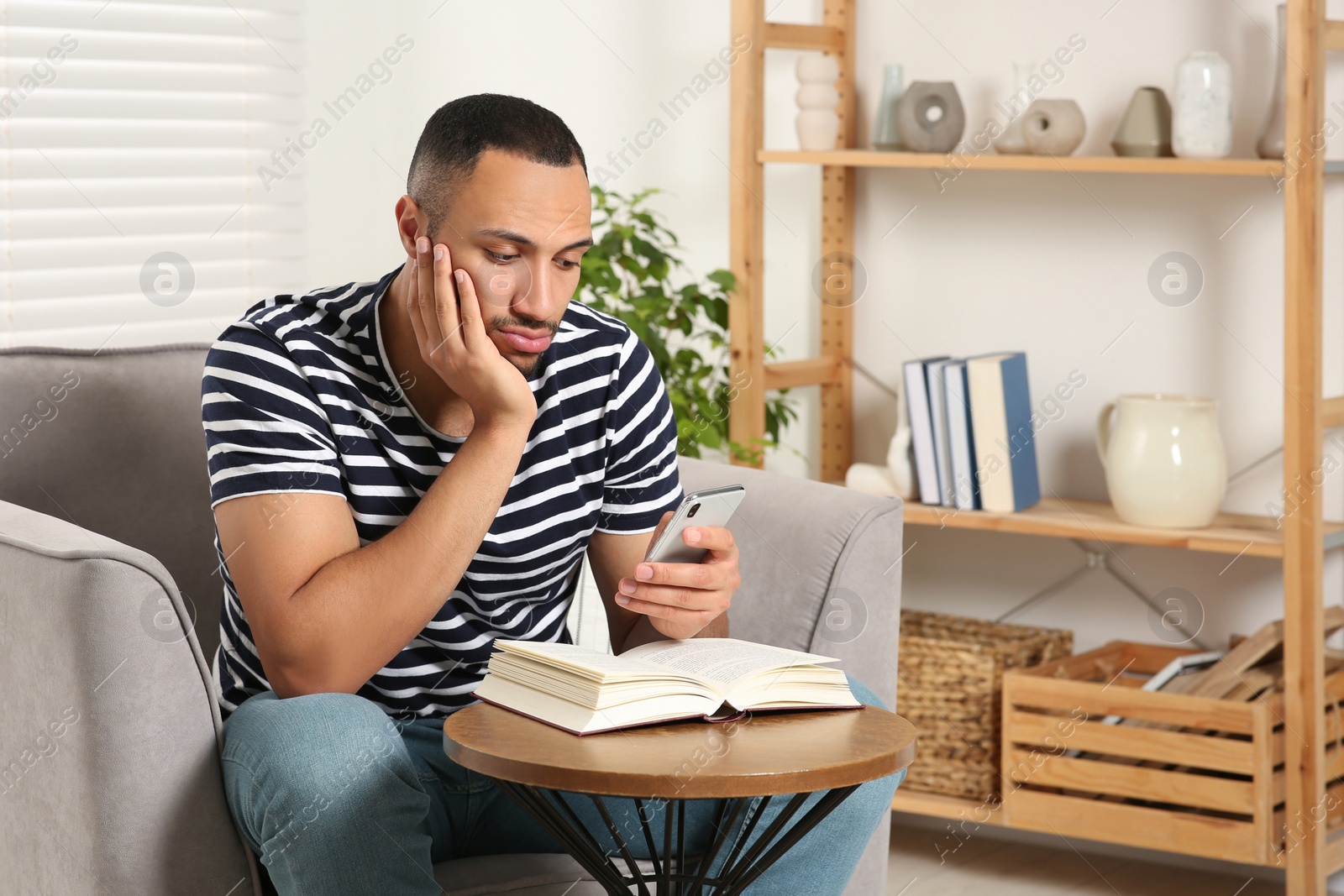 Photo of Young man using smartphone while reading book at home. Internet addiction