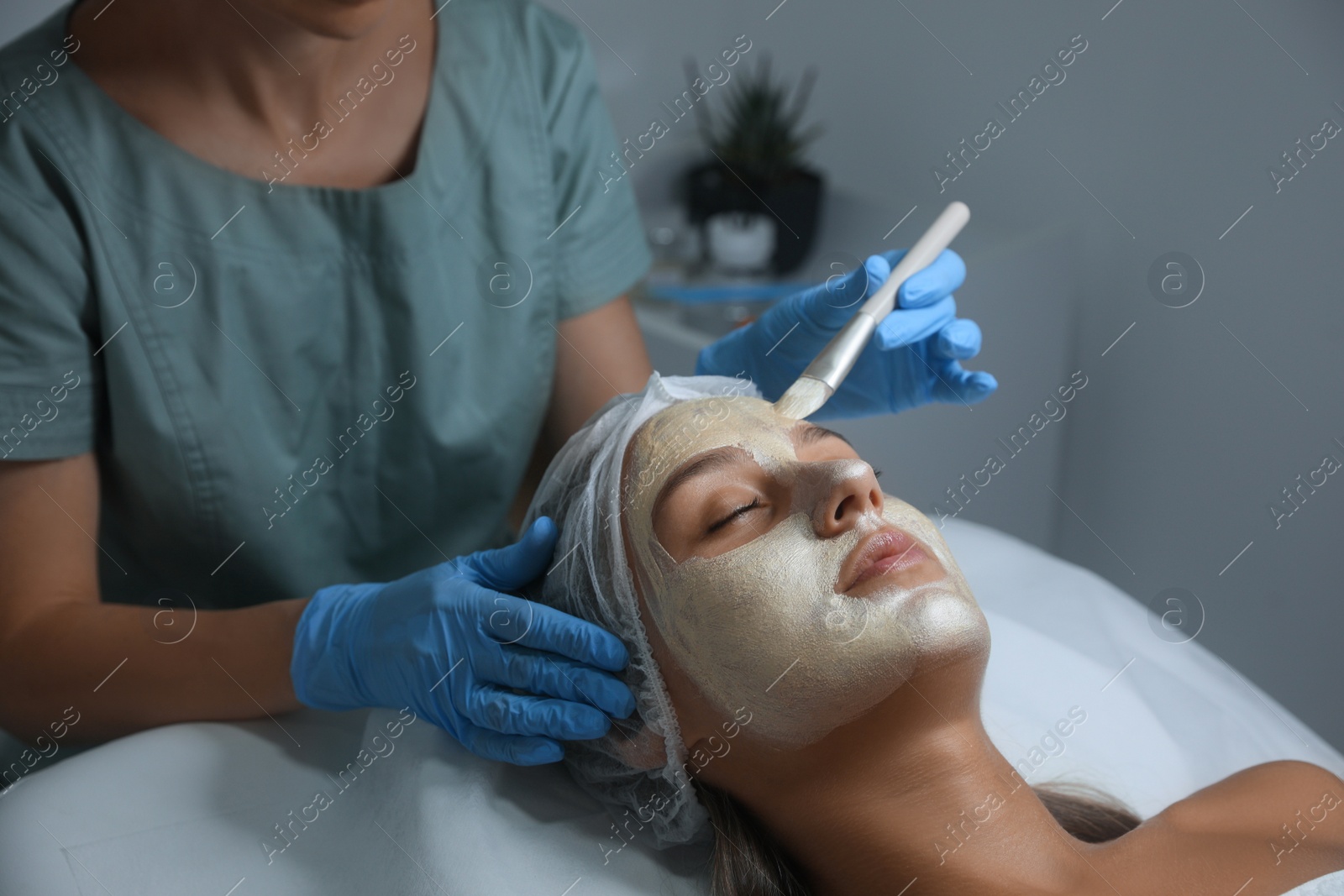 Photo of Cosmetologist applying mask on client's face in spa salon