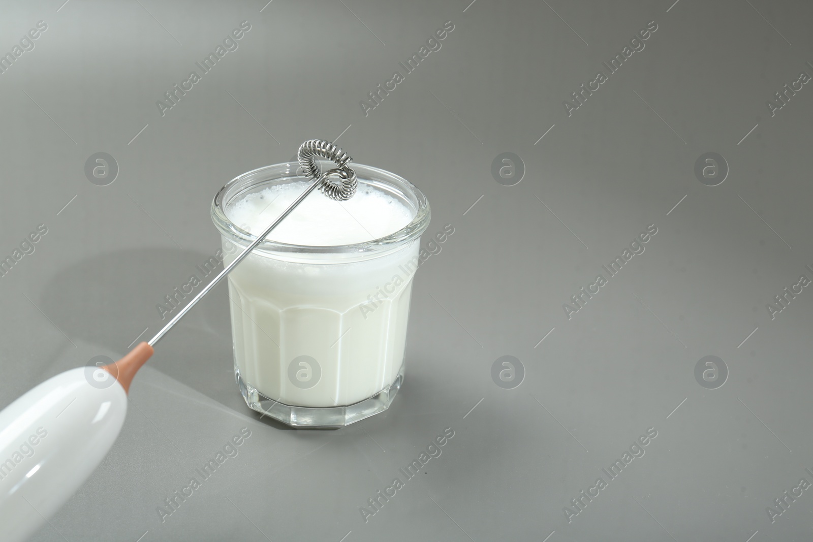 Photo of Mini mixer (milk frother) and whipped milk in glass on grey background. Space for text