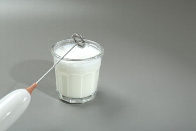 Mini mixer (milk frother) and whipped milk in glass on grey background. Space for text