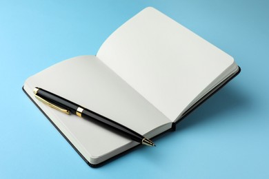 Photo of Open notebook with blank pages and pen on light blue background