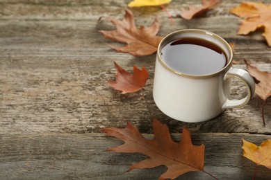 Cup of hot tea and autumn leaves on wooden table, space for text