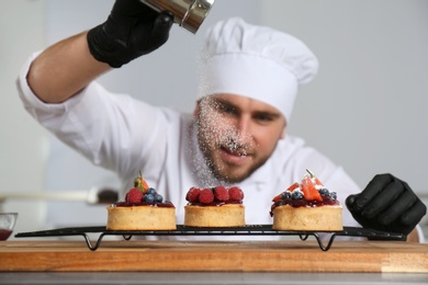Photo of Male pastry chef sprinkling desserts with sugar powder in kitchen
