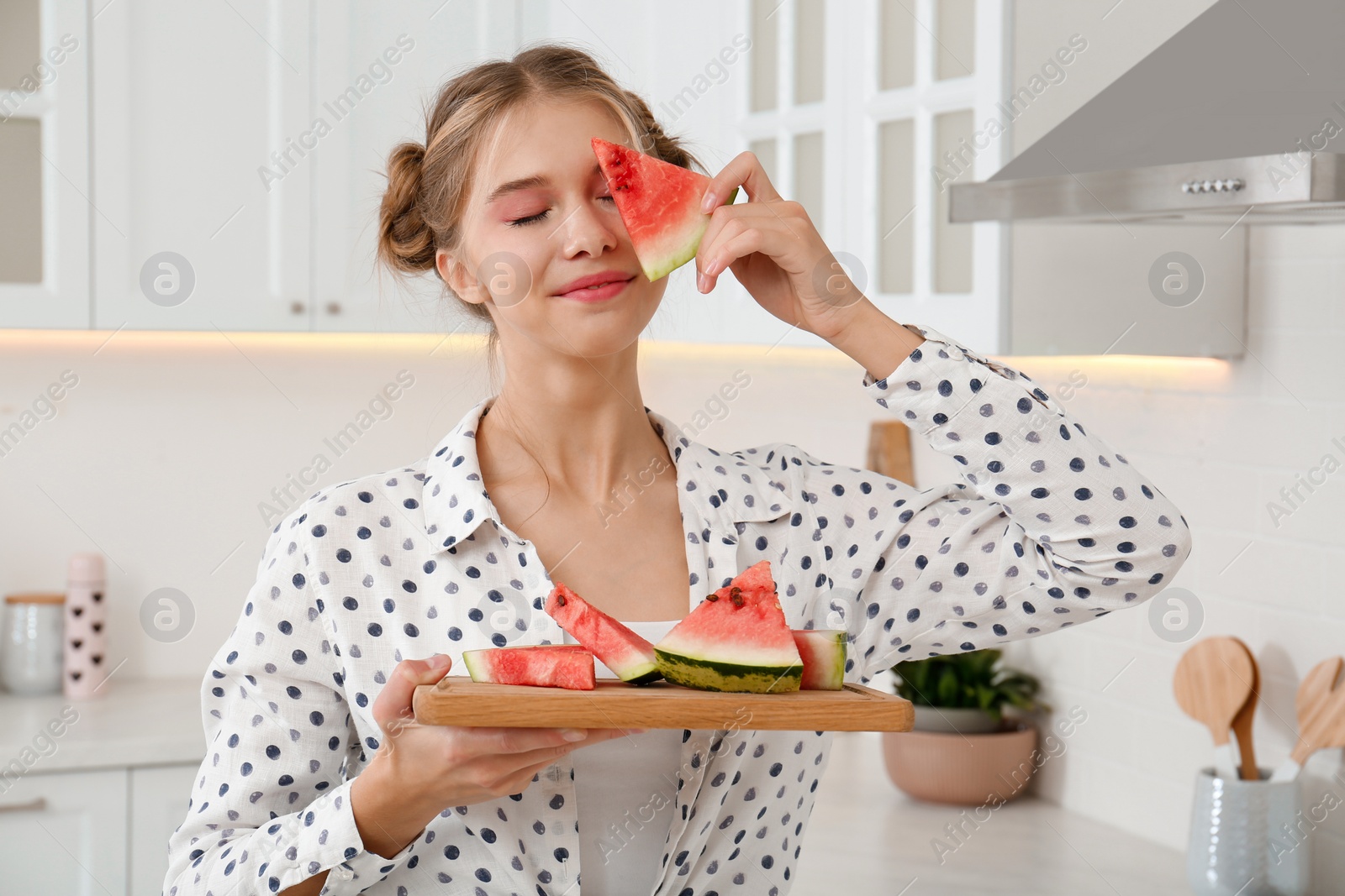 Photo of Beautiful teenage girl with slices of watermelon in kitchen