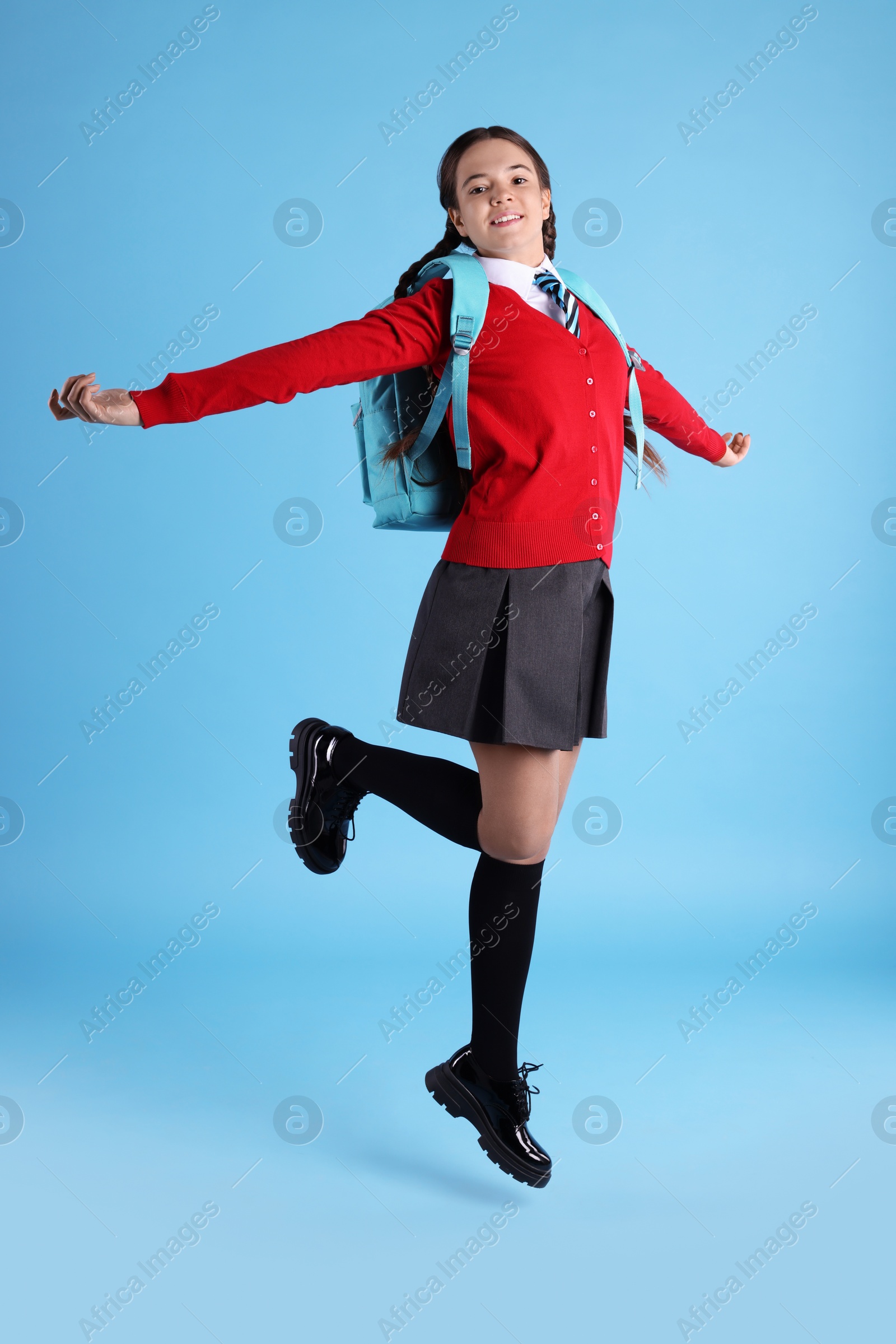 Photo of Teenage girl in school uniform with backpack jumping on light blue background