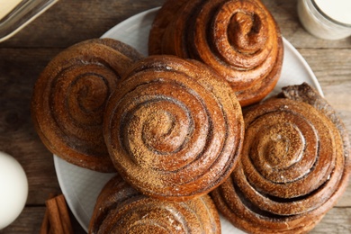 Plate with baked cinnamon rolls on wooden table, top view