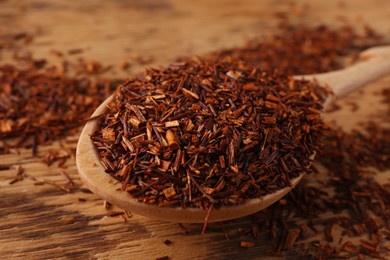 Photo of Spoon with dry rooibos leaves on wooden table, closeup