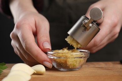 Woman squeezing garlic with press at wooden table, closeup