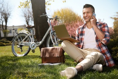 Photo of Man with laptop talking on phone in park