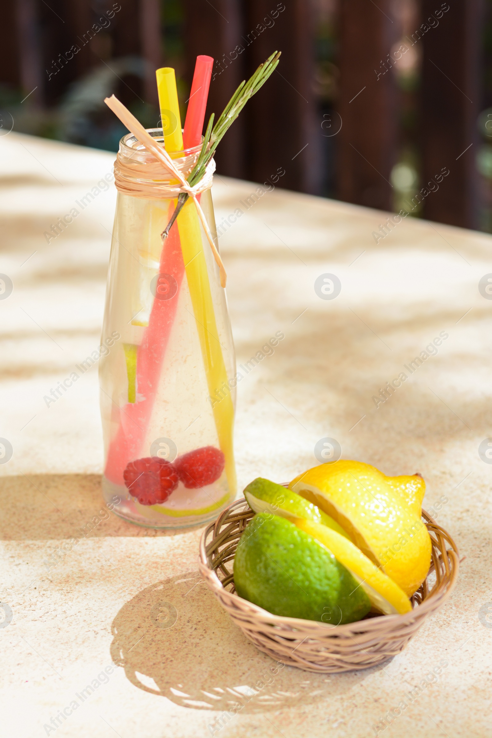 Photo of Refreshing tasty lemonade served in glass bottle and citrus fruits on beige table