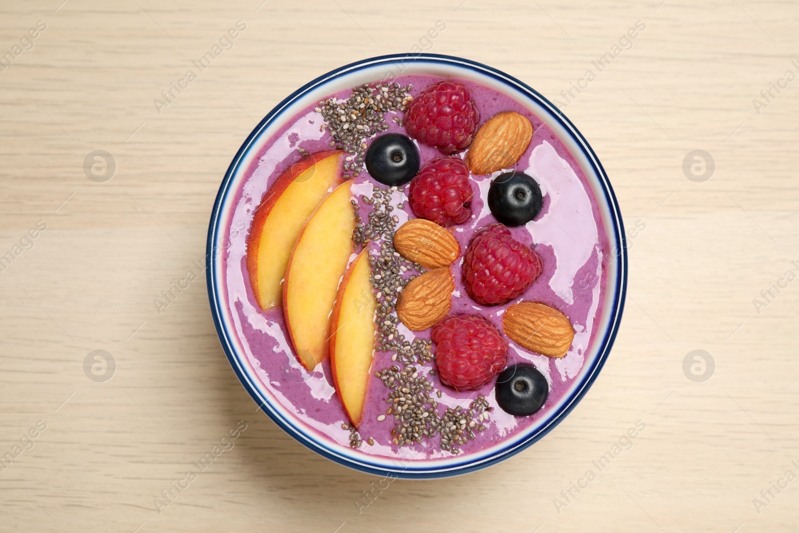 Photo of Delicious acai smoothie with fruits and almonds in bowl on wooden table, top view