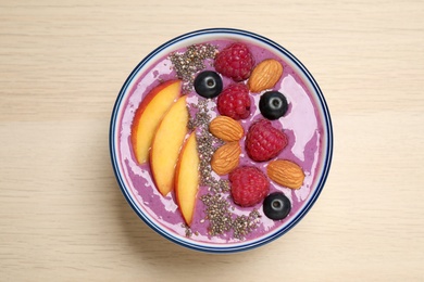 Delicious acai smoothie with fruits and almonds in bowl on wooden table, top view