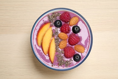 Photo of Delicious acai smoothie with fruits and almonds in bowl on wooden table, top view