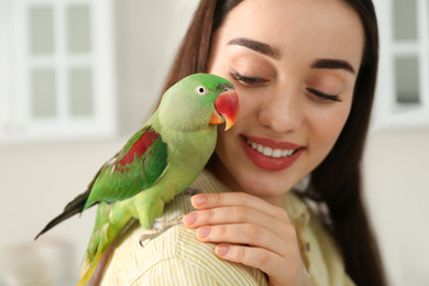 Photo of Young woman with Alexandrine parakeet indoors, closeup. Cute pet