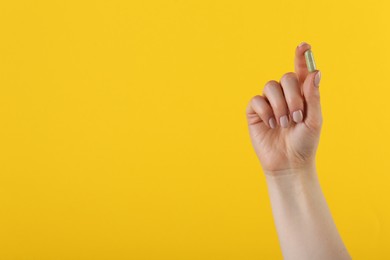 Photo of Woman holding vitamin capsule on yellow background, closeup with space for text. Health supplement