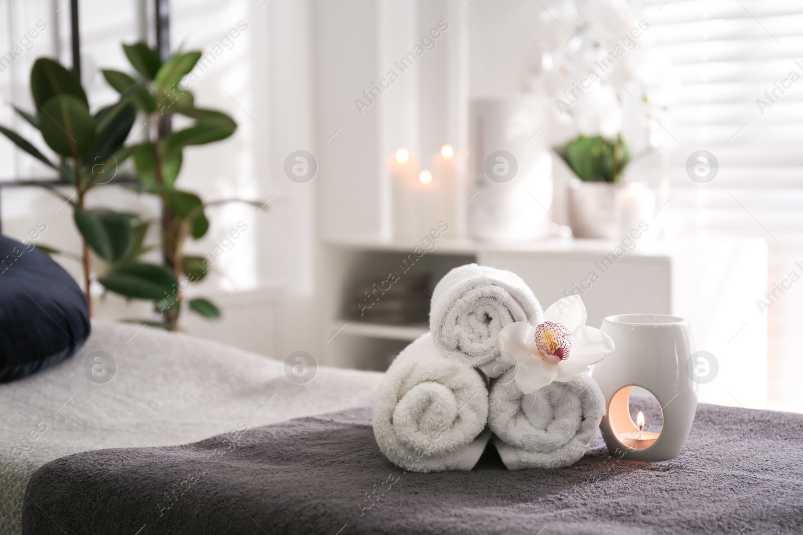 Photo of Towels, aroma lamp and orchid flower on couch in spa salon