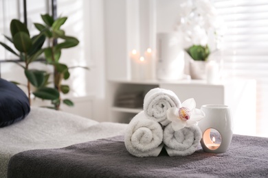 Photo of Towels, aroma lamp and orchid flower on couch in spa salon