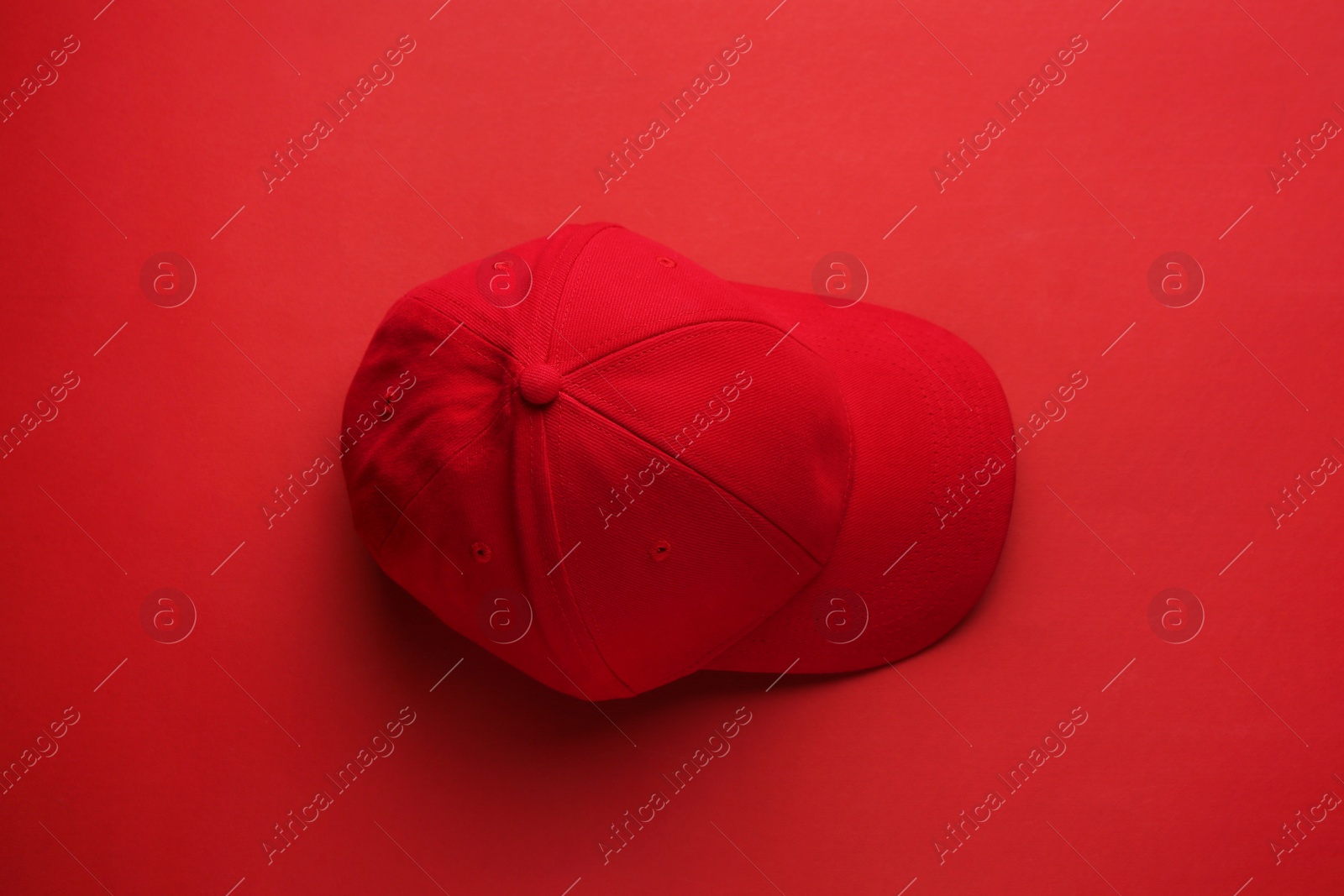 Photo of Stylish red baseball cap on color background, top view