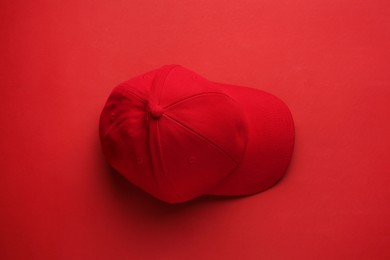 Stylish red baseball cap on color background, top view