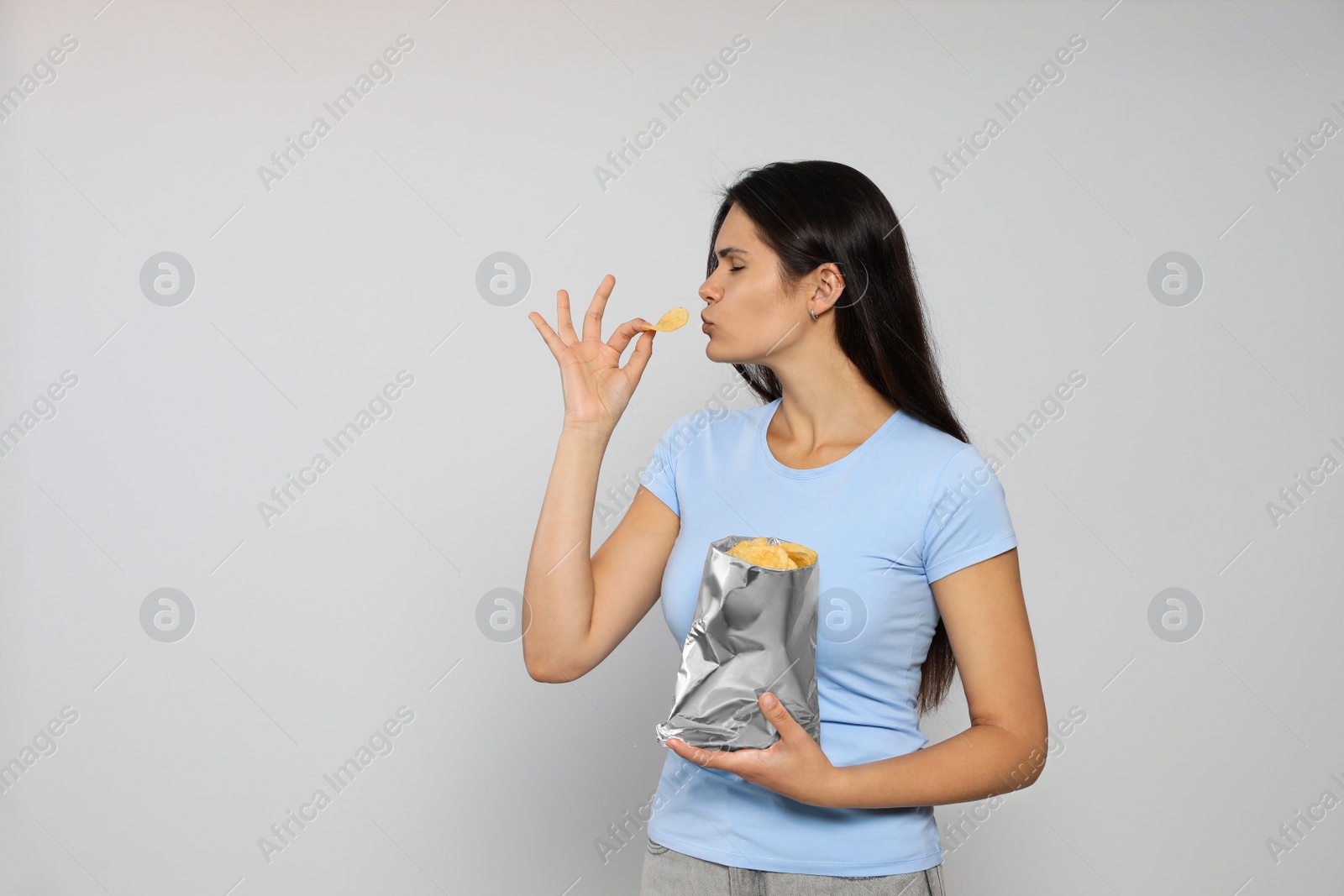 Photo of Beautiful woman eating potato chips on grey background. Space for text