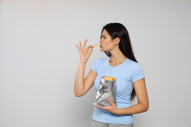 Beautiful woman eating potato chips on grey background. Space for text