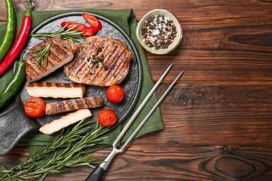 Photo of Grilled pork steaks with rosemary, spices, vegetables and carving fork on wooden table, top view. Space for text