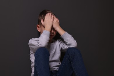 Photo of Child abuse. Upset boy near gray wall