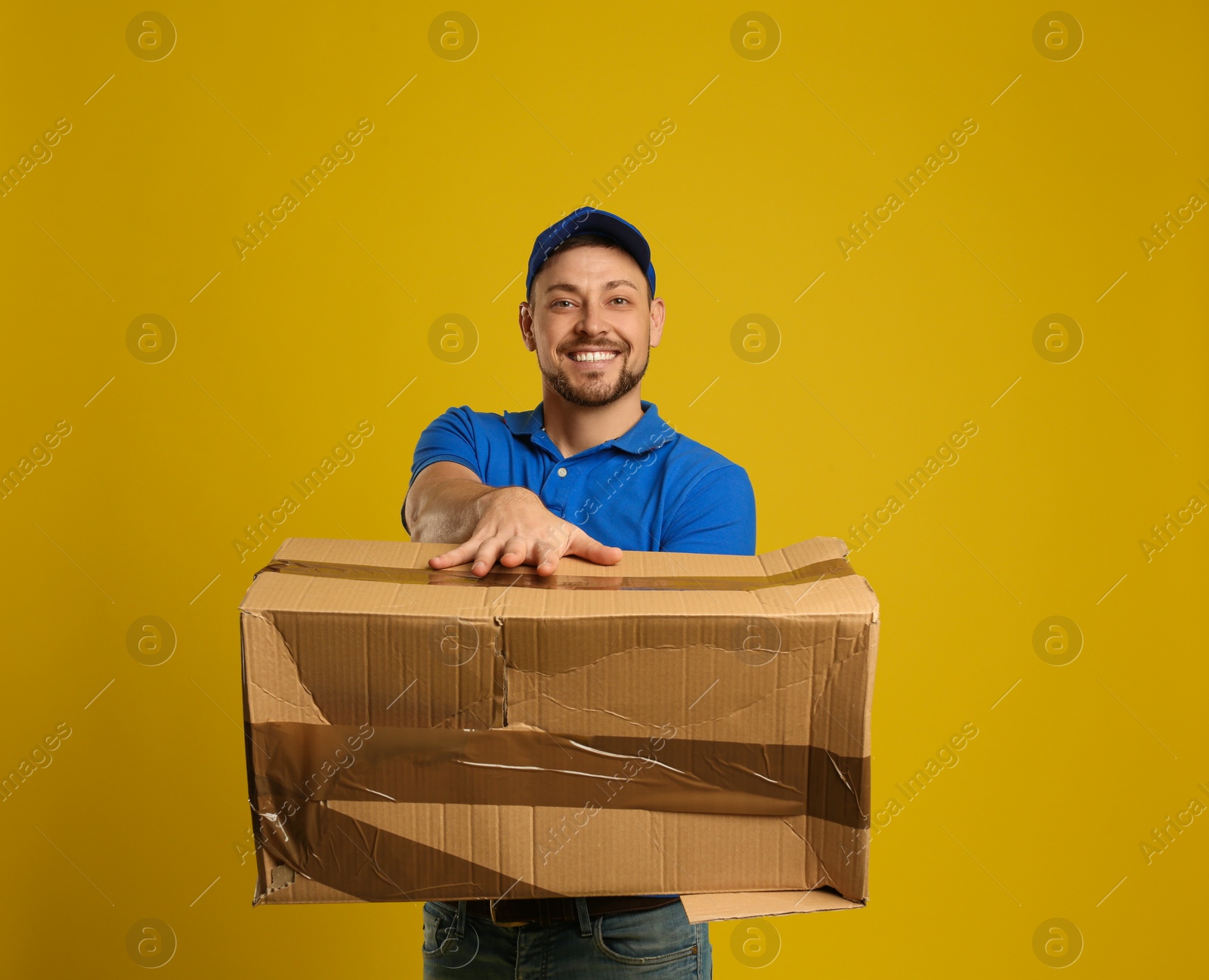 Photo of Courier with damaged cardboard box on yellow background. Poor quality delivery service