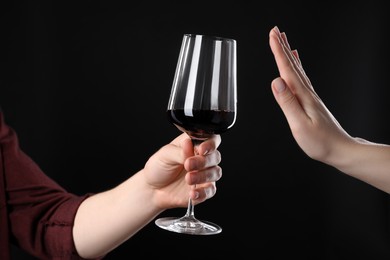 Photo of Alcohol addiction. Woman refusing glass of wine on black background, closeup