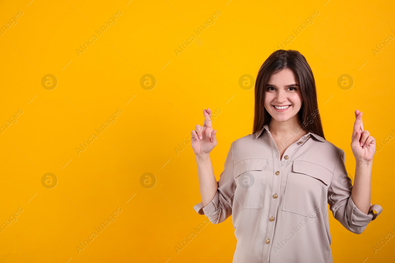 Photo of Happy young woman crossing fingers on yellow background, space for text. Dealing with stress