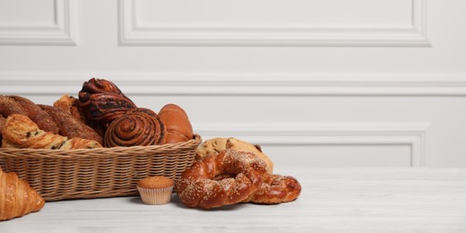 Wicker basket with different tasty freshly baked pastries on white wooden table, space for text