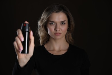 Young woman using pepper spray on black background