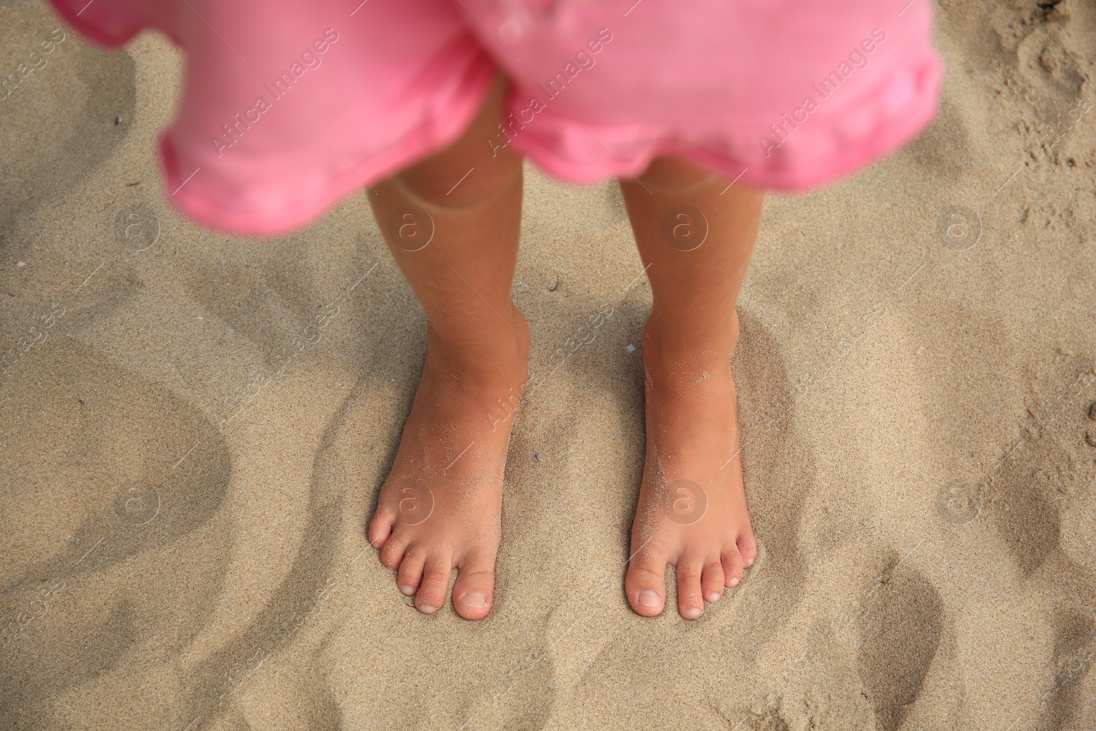 Photo of Little girl standing on sandy beach, closeup