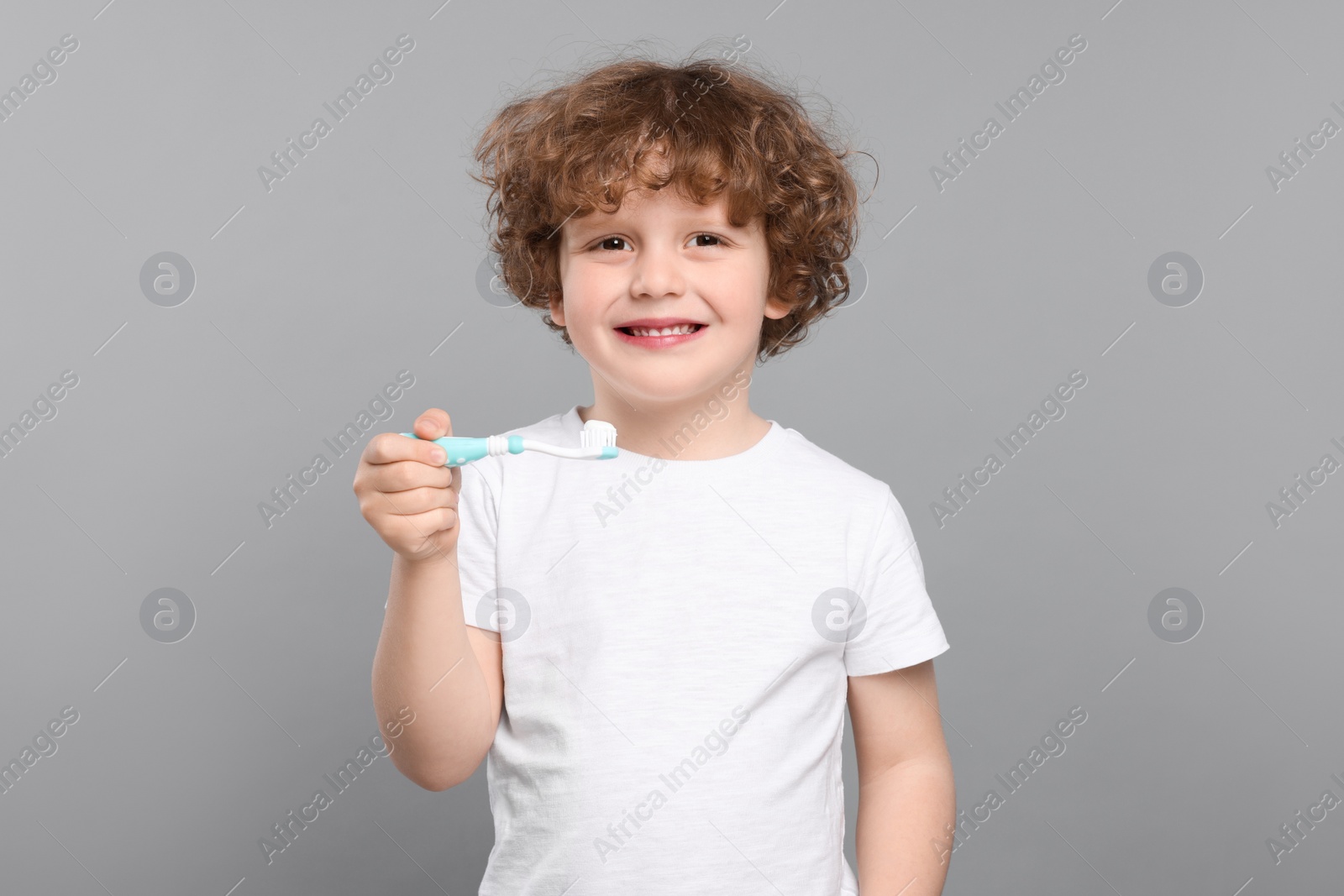 Photo of Cute little boy holding plastic toothbrush with paste on light grey background